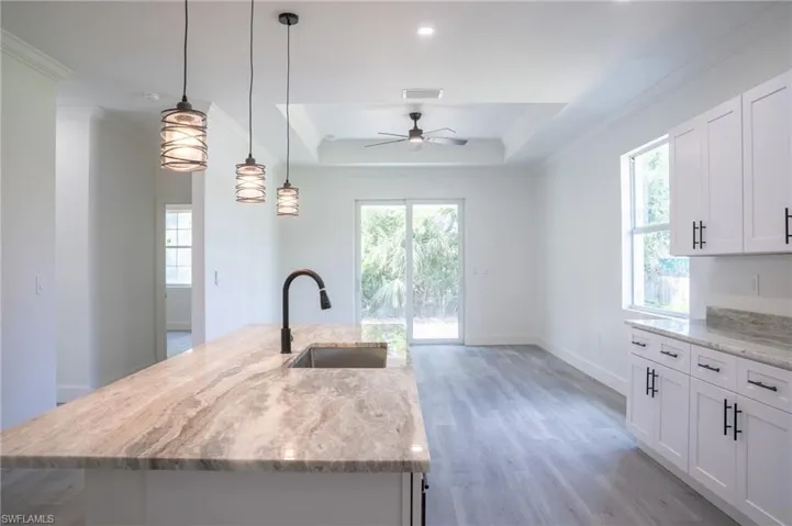 Kitchen with light stone countertops, hanging light fixtures, light wood-style flooring, white cabinets, and an island with sink