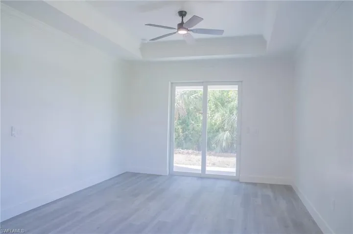 Empty room featuring a raised ceiling, ornamental molding, light wood finished floors, and ceiling fan