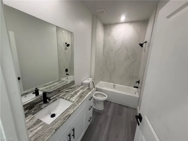 Bathroom with vanity, bathtub / shower combination, and dark wood-style flooring