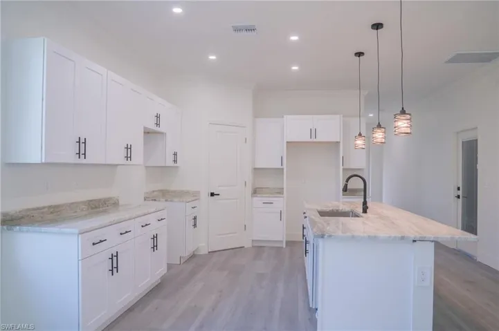 Kitchen with white cabinets, light wood-type flooring, decorative light fixtures, ornamental molding, and recessed lighting