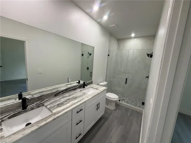 Bathroom with a marble finish shower, double vanity, and dark wood-style flooring