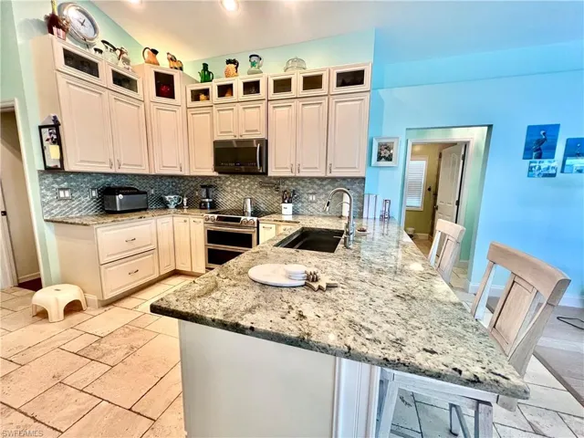 Kitchen featuring QUARTZ countertops, decorative backsplash, a breakfast bar, and appliances with stainless steel finishes with TRAVERTINE stone tile floors.