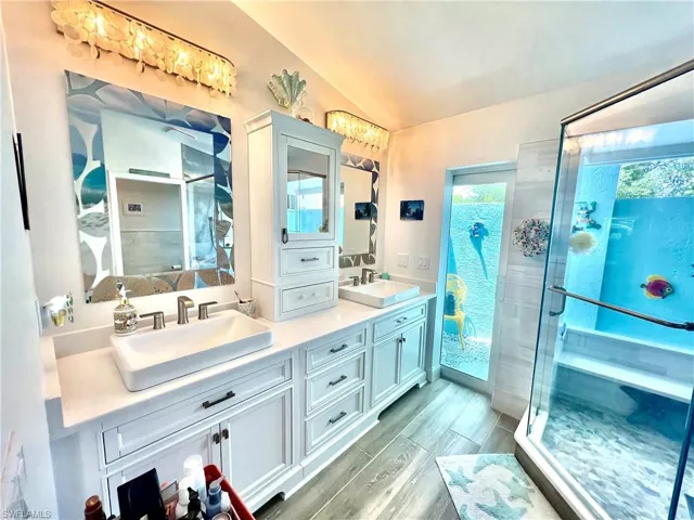 Primary bathroom with dual vessel sinks, plenty of cabinet space, frameless glass shower door and luxury vinyl plank floors overlooking the atrium.