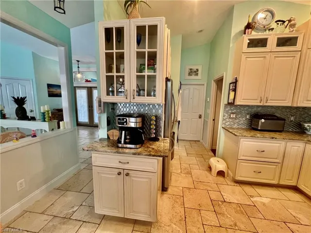 Kitchen with coffee bar, decorative backsplash, TRAVERTINE tile floors, and glass insert cabinets