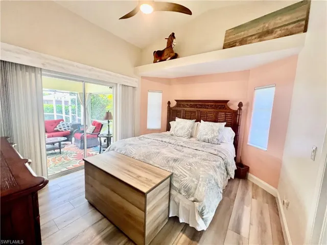 Primary bedroom with luxury vinyl plank floors, cathedral ceilings, decorative plant shelves and access to the pool area.
