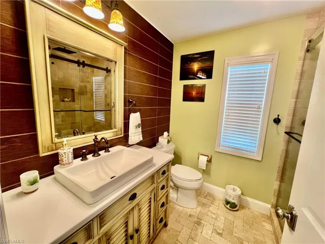 Full bathroom with toilet, decorative tile walls, baseboards, walk in shower, and vanity with vessel sink.