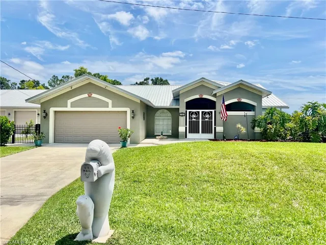 Ranch-style home with driveway, metal roof, an attached garage, a front yard, and stucco siding