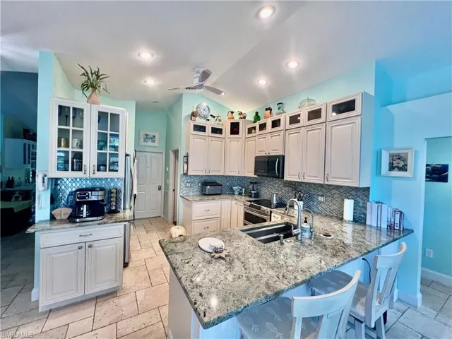 Kitchen featuring a breakfast bar, a sink, backsplash, a coffee bar, and cathedral ceilings with plant shelves.
