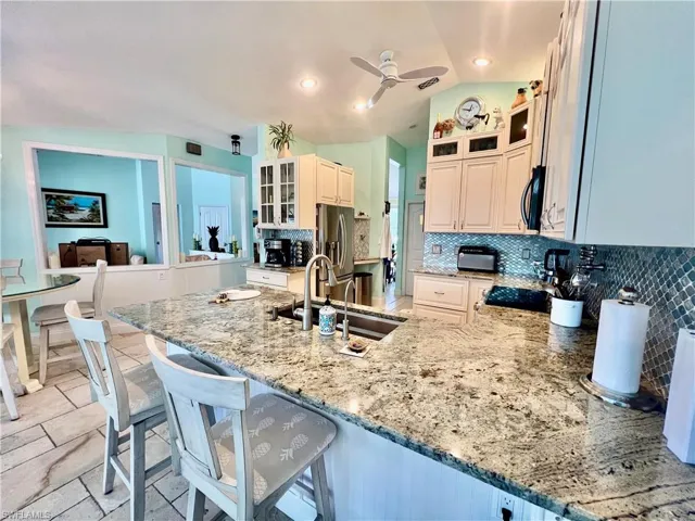 Kitchen featuring QUARTZ countertops, decorative backsplash, a breakfast bar, and appliances with stainless steel finishes with TRAVERTINE stone tile floors.