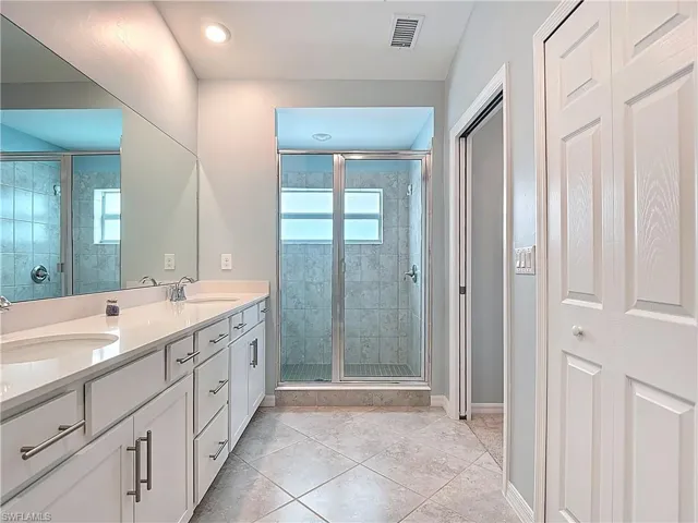 Bathroom with a stall shower, light tile patterned flooring, and double vanity