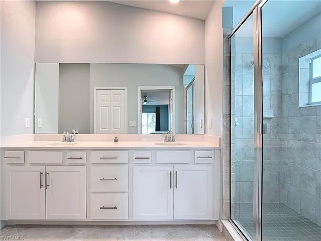 Bathroom with a shower stall, double vanity, a ceiling fan, and light tile patterned floors