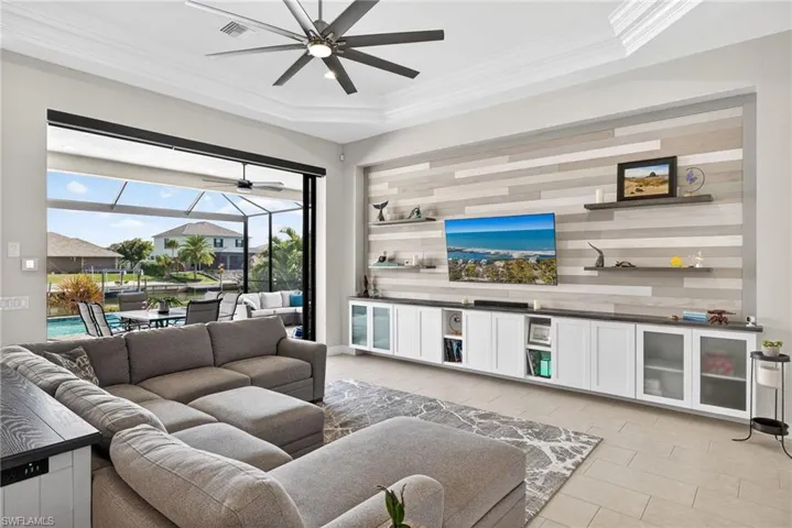 Living area custom entertainment wall, crown molding, a ceiling fan, and a tray ceiling