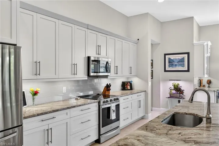 Kitchen featuring stainless steel appliances, white cabinetry, light stone counters, and backsplash