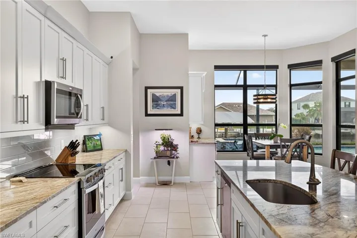 Kitchen with stainless steel appliances, a breakfast bar, light stone countertops, an island with sink, and white cabinets with under and upper cabinet lighting