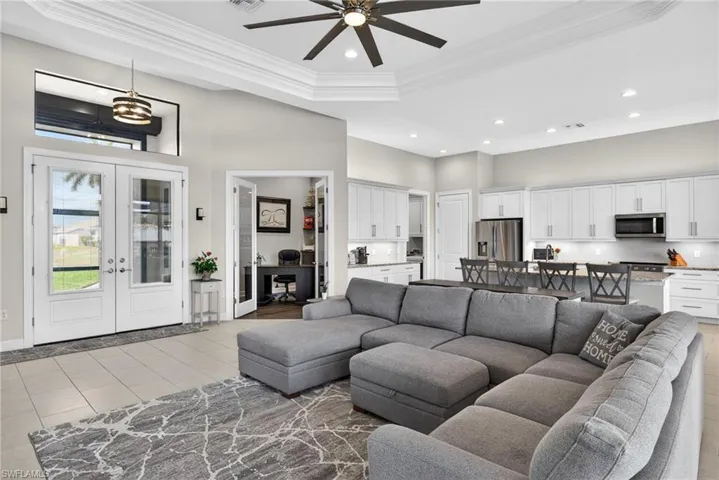 Living room with french doors, ornamental molding, ceiling fan, a tray ceiling, and suspended lighting.