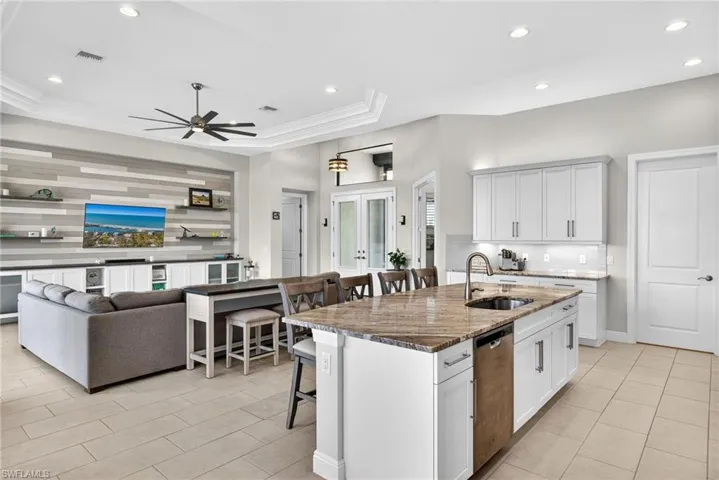 Kitchen with open floor plan, a kitchen breakfast bar, dark stone counters, decorative backsplash, and undercabinet lighting