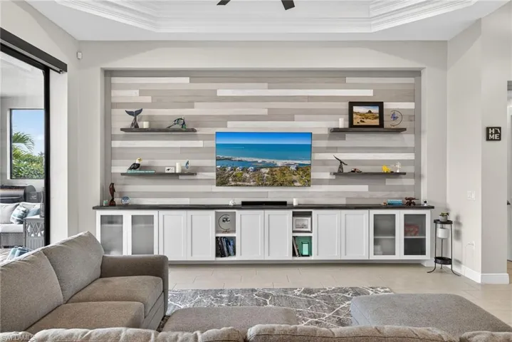 Living room featuring a custom wall with built in cabinets, crown molding, a raised ceiling, and ceiling fan
