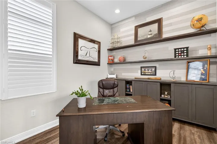 Home office with dark wood-style flooring and a custom wall with built in cabinets