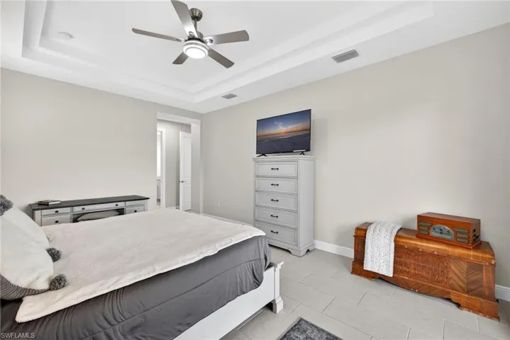 Primary bedroom with access to outside, ceiling fan, a tray ceiling, and light tile patterned flooring