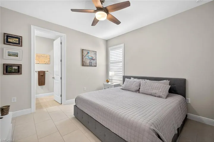 Bedroom with light tile patterned floors, ceiling fan, and ensuite bath