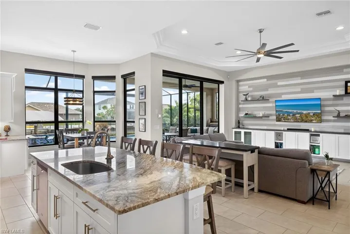 Kitchen with light stone countertops, open floor plan, white cabinetry, a breakfast bar area, and a raised ceiling