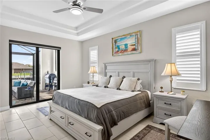 Bedroom featuring a tray ceiling, access to exterior, multiple windows, ceiling fan, and light tile patterned flooring