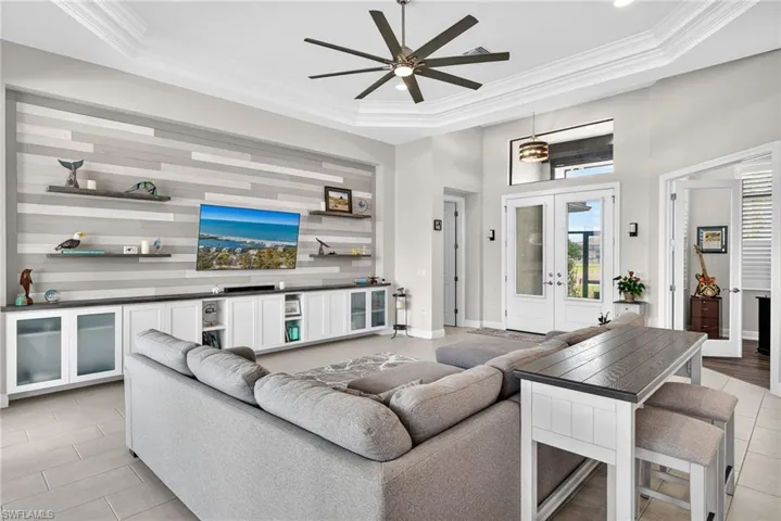 Living room featuring custom wall with built in cabinets, french doors, ornamental molding, a ceiling fan, and a tray ceiling
