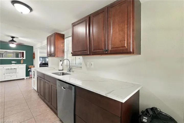 Kitchen featuring dark wood-finish cabinetry, stone-patterned countertops, a stainless steel dishwasher, an undermount sink, and tiled flooring