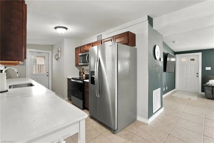 Kitchen featuring white countertops, wood-finish cabinetry, stainless steel side-by-side refrigerator, over-the-range microwave, and tile flooring