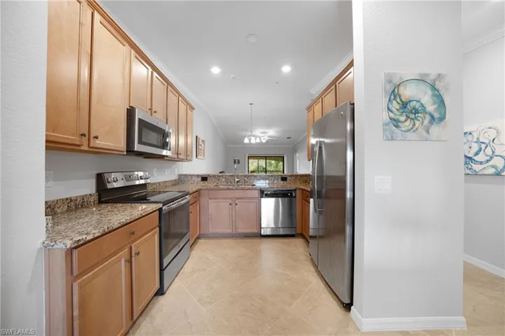 Kitchen with light stone counters, appliances with stainless steel finishes, crown molding, hanging light fixtures, and light tile patterned floors