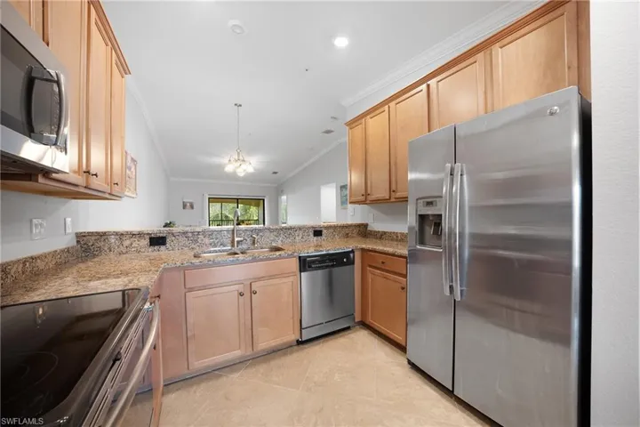 Kitchen featuring appliances with stainless steel finishes, ornamental molding, light stone countertops, a chandelier, and decorative light fixtures