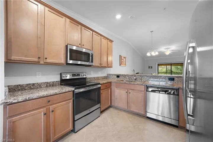 Kitchen featuring stainless steel appliances, light stone countertops, crown molding, vaulted ceiling, and a chandelier