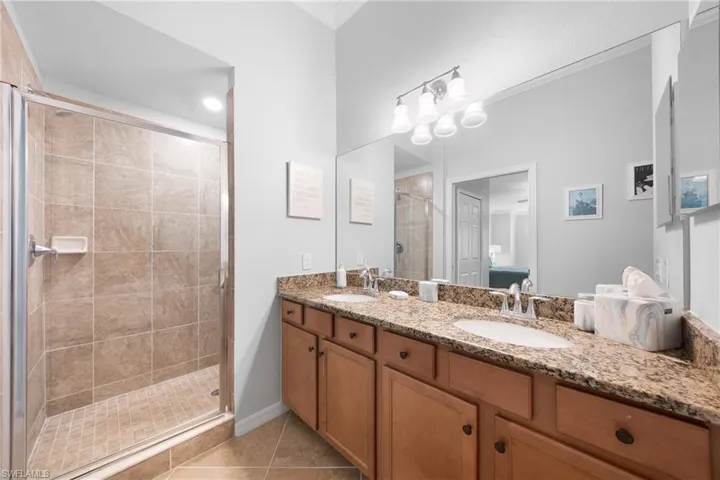 Full bathroom featuring a shower stall, double vanity, light tile patterned floors, and crown molding