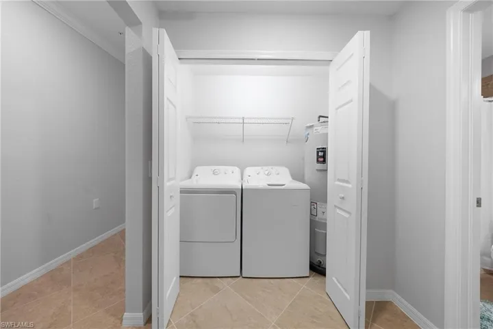 Laundry room featuring washer and clothes dryer, water heater, and light tile patterned floors