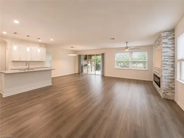 Open-concept living space featuring wood-finish flooring, a kitchen island with pendant lighting, a stone-clad fireplace with an integrated media niche, and sliding glass doors to the exterior
