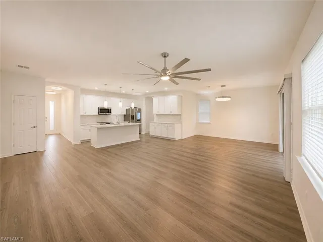 Open-concept living space featuring wood-finish flooring, white kitchen cabinetry, a kitchen island, and a ceiling fan