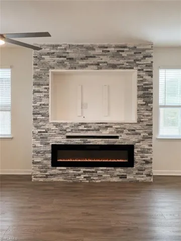 Stacked stone accent wall with integrated linear electric fireplace, wood-finish flooring, and a ceiling fan
