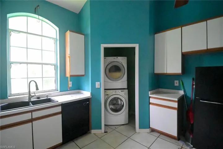 Clothes washing area featuring sink, stacked washer and clothes dryer, and light tile patterned floors