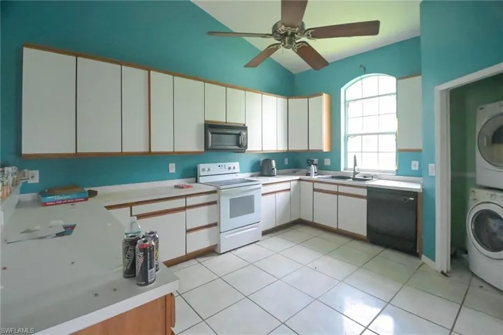 Kitchen with black appliances, stacked washer and clothes dryer, sink, and white cabinetry