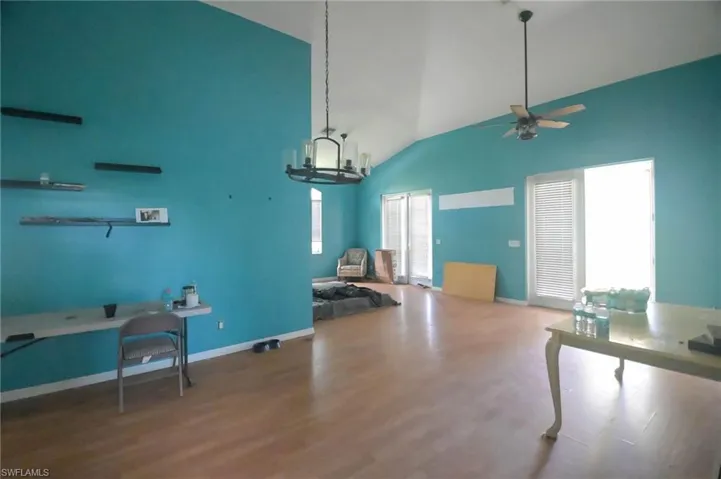 Living room with high vaulted ceiling, ceiling fan with notable chandelier, and hardwood / wood-style flooring