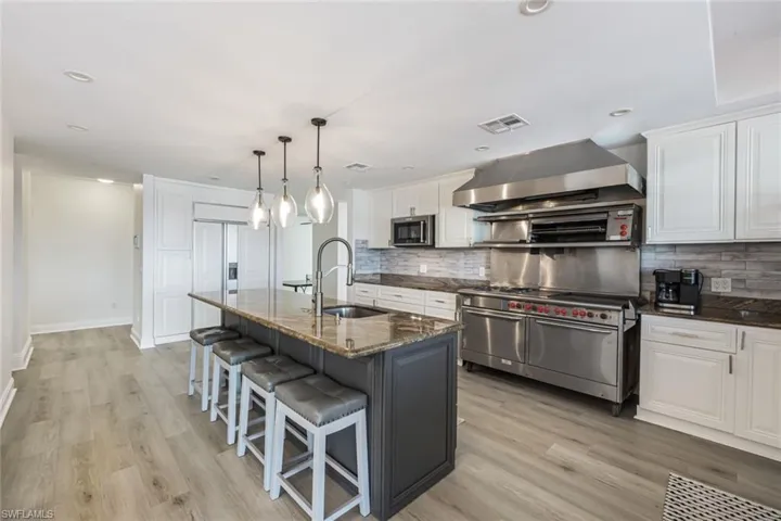 Kitchen with tasteful backsplash, an island with sink, wall chimney range hood, sink, and appliances with stainless steel finishes