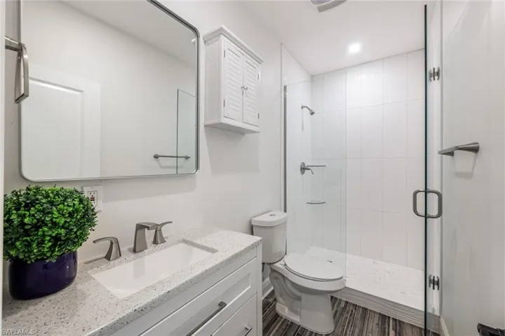 Bathroom with walk in shower, vanity, toilet, and wood-type flooring