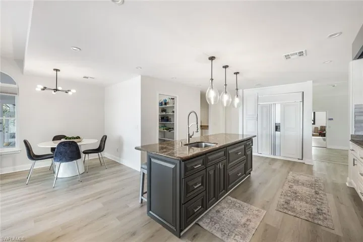 Kitchen featuring light hardwood / wood-style floors, hanging light fixtures, a kitchen island with sink, dark stone countertops, and sink