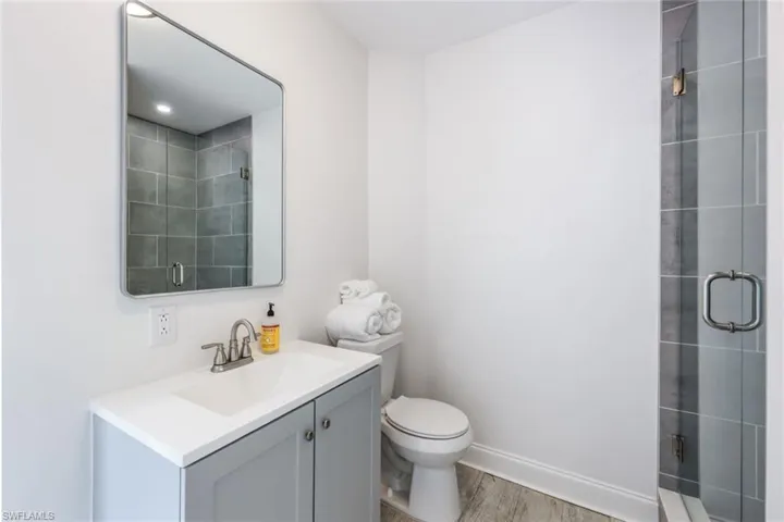 Bathroom featuring a shower with shower door, vanity, toilet, and wood-type flooring
