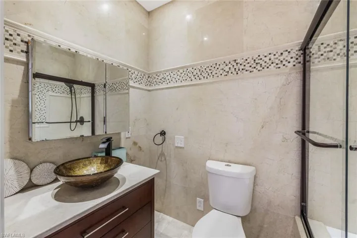 Bathroom with tile walls, walk in shower, vanity, and toilet