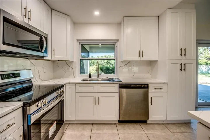 Kitchen with stainless steel appliances, white cabinets, light stone countertops, light tile patterned floors, and recessed lighting