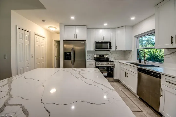 Kitchen featuring stainless steel appliances, light stone counters, white cabinetry, tasteful backsplash, and recessed lighting
