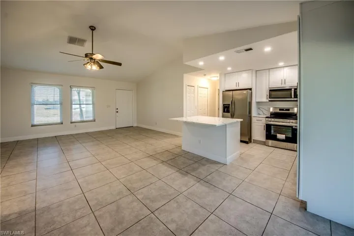 Kitchen featuring a kitchen island, stainless steel appliances, white cabinetry, lofted ceiling, and light tile patterned floors