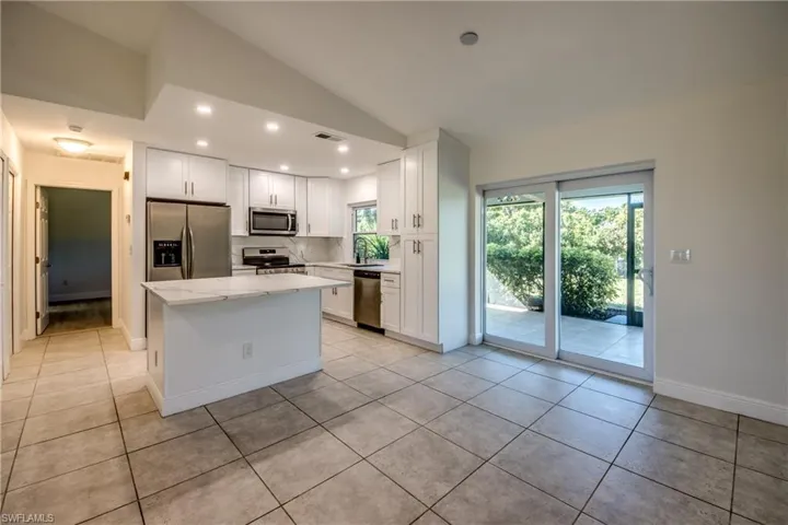 Kitchen featuring appliances with stainless steel finishes, lofted ceiling, white cabinetry, a center island, and light tile patterned floors