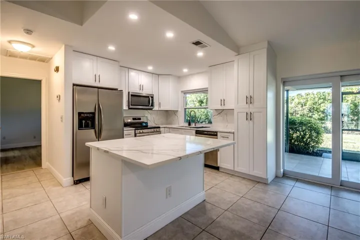 Kitchen with stainless steel appliances, white cabinets, light tile patterned flooring, light stone counters, and a center island